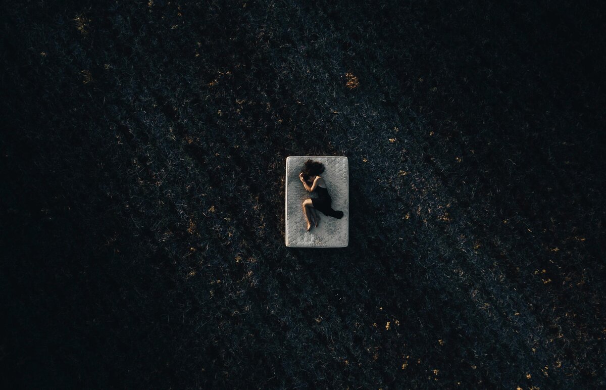 Aerial perspective of isolated figure on white mattress surrounded by dark autumn leaves